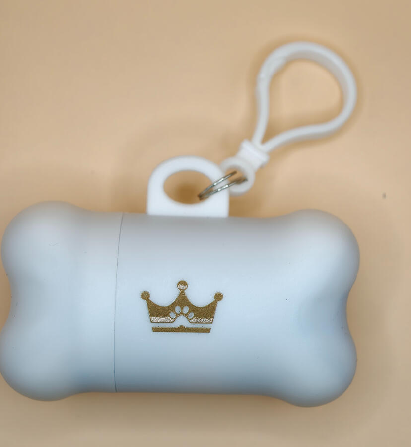 Weisser ROYA Kotbeutelspender in Knochenform mit goldenem Kronenlogo und Befestigungsschlaufe für die Hundeleine.